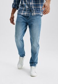 Jasnoniebieskie dżinsy o luźnym kroju, z subtelnymi przetarciami i bocznymi kieszeniami, w połączeniu z białymi sneakersami i niebieską koszulą w kratę.