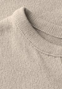 Světle béžový pletený svetr s kulatým výstřihem, který má texturovaný vzor a ribbovaný límec. Materiál vypadá měkce a teple.