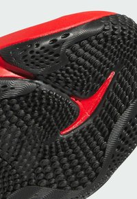 Schwarze Sportschuhsohle mit einer strukturierten Oberfläche, die kleine erhabene Kreise und einen auffälligen roten Nike Swoosh-Akzent aufweist.
