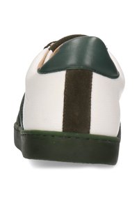 Zapatilla blanca con acentos en verde y marrón, materiales texturizados, suela plana y un talón acolchado. Presenta una franja oscura vertical en la parte trasera.