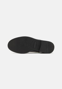 Suela de zapato negra con un patrón de agarre texturizado, con un borde liso y un detalle mínimo. Material de goma con un diseño robusto.