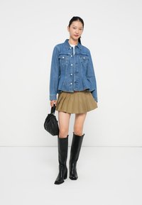 Denimjakke med strukturert passform, lyseblå farge, to brystlommer, kombinert med en plissert beige skjørt og svarte knelengde støvler.