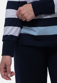 Långärmad topp med marinblå, vit och ljusblå horisontella ränder. Mjuk bomullstyg med ribbade ärmslut, lös passform och rundad nederkant.