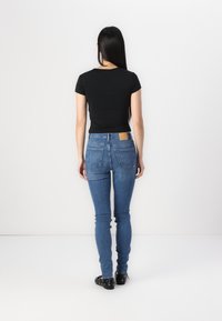 Fekete, testhez simuló póló és kék skinny farmer, hátul zsebekkel. A farmer világos mosott és egy bézs bőr folt található a deréknál. Fekete lábbeli látható.