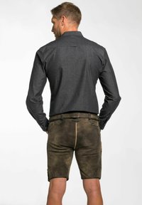 Donkergrijze lange mouwen shirt met een knoopsluiting kraag, gecombineerd met bruine suède shorts met zakken en een bruine riem.