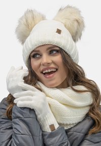 Białe dzianinowe beanie z dwoma dużymi pomponami z sztucznego futra, w komplecie z dopasowanymi rękawicami i teksturowanym szalikiem, wszystko w miękkim białym materiale.