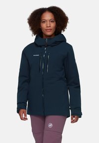Navy blue softshell jacket featuring a hood, zippered pockets, and subtle branding. Made from durable, textured fabric for outdoor wear.