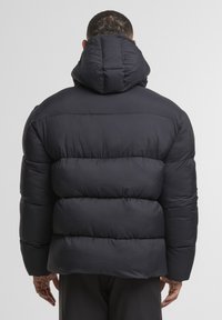 Dunjakke i svart med hette, som har et quiltet design med tydelige horisontale seksjoner for isolasjon og en jevn tekstur.