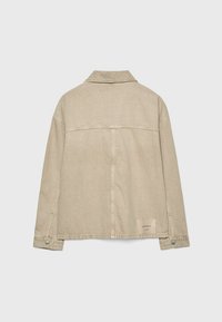 Veste en denim beige avec un col, des manches longues et une coupe carrée. Présente des détails de couture au dos et une étiquette en tissu sur l'ourlet inférieur.