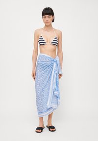 Bikini med svart og hvit striper, kombinert med et blått mønstret sarong knyttet i midjen, og svarte sandaler.