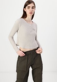 Beige stripete topp med lange ermer, rund hals og knappedetaljer, kombinert med mørkegrønne cargo-bukser med sidesyninger og flere lommer.
