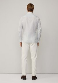 Herren Langarmhemd in Hellblau mit kleinem Karomuster, ausgestattet mit einem klassischen Kragen und knöpfbaren Manschetten, kombiniert mit weißen Hosen.