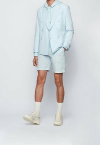 Blazer ajustado de color azul claro, sudadera con capucha azul claro, pantalones cortos a juego y zapatillas beige. Tela suave, diseño de doble botonadura, acentos mínimos.