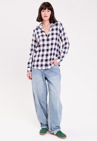 Chemise à carreaux bleu marine et blanche à manches longues, assortie à un jean en denim léger à jambe large et des baskets vertes.