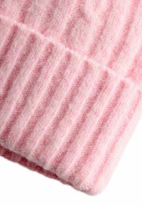 Bonnet en tricot rose avec une texture côtelée. Le matériau semble doux et flou, présentant des lignes surélevées et plates alternées.