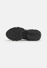 Semelle de chaussure de sport noire avec des profondes rainures, présentant un motif texturé pour l'adhérence et une section centrale lisse. Fabriquée en matériau en caoutchouc.