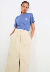 Tricou din bumbac albastru cu un buzunar pe piept, asortat cu o fustă bej până la genunchi, cu un fermoar frontal și buzunare laterale.
