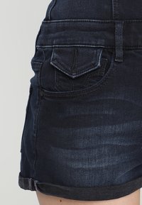 Tmavě modré džíny s přiléhavým střihem, které mají přední kapsy, šité detaily a ohrnutý lem pro uvolněný vzhled.