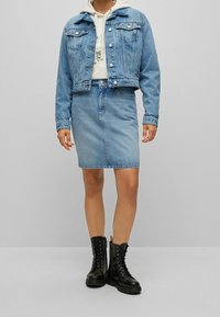 Chaqueta vaquera con botones metálicos, diseño cropped y color azul claro. Combinada con una falda vaquera a juego y botas negras con cordones.