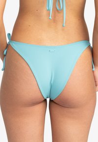 Ljust blå bikiniunderdel med knytband på sidorna, tillverkad av ett mjukt material; har en låg midja och en liten logotypdetalj på baksidan.