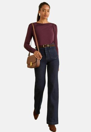 Långärmad vinröd topp med rynkade axeldetaljer, högmidjade mörkjeans med utsvängda ben, brun bälte och brun axelväska.