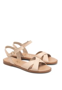 Beżowe skórzane sandały z krzyżowym paskiem, otwartym palcem, regulowanym paskiem na kostkę i płaską brązową podeszwą. Prosty i funkcjonalny styl.