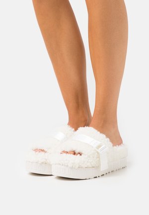 Puszyste białe klapki na platformie, wykonane z miękkiego materiału z owczej wełny, z błyszczącym białym paskiem z logo.