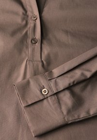 Braun-kariertes Hemd mit Knopfleiste und zwei Knöpfen, langen Ärmeln mit geknöpften Manschetten, aus glattem, strukturiertem Stoff.