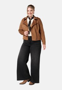 Bruine faux suède motorjack, zwarte wijde jeans, tan enkellaarzen, witte sweater, zwart en gouden patroon sjaal, casual outfit.