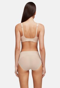 Conjunto de sujetador inalámbrico beige y bragas de cintura alta. Textura suave, tirantes ajustables y costuras sutiles para mayor comodidad y ajuste.