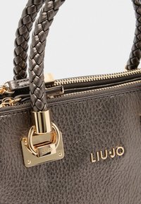 Un sac à main en cuir noir texturé avec des poignées tressées et du matériel en or, comprenant un logo en relief et un détail de fermeture éclair.