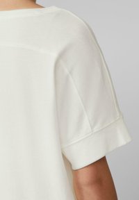 Krótki rękaw biały t-shirt o luźnym kroju, wykonany z miękkiej bawełny, z podwiniętymi rękawami. Widać szwy na ramionach.