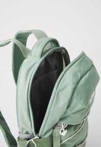 Sac à dos vert avec une texture matelassée, doté d'une ouverture zippée, de bretelles rembourrées et d'une doublure intérieure, adapté à divers usages.