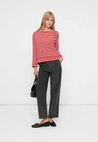 Red and white striped long-sleeve top paired with olive green wide-leg trousers and black flats, accompanied by a small black handbag.