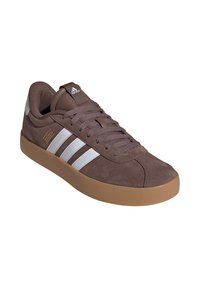 Sneaker in suede marrone con tre strisce bianche, suola in gomma e lacci grigi. Presenta un design cucito e un collo imbottito per il comfort.