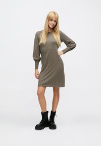 Sukienka dzianinowa w miękkim brązowym materiale, z długimi bufkowymi rękawami i prostą sylwetką, zestawiona z czarnymi sznurowanymi butami wojskowymi.