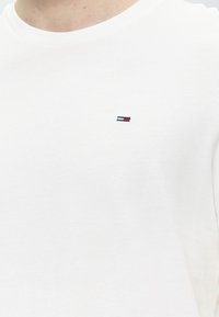 Λευκό T-shirt με στρογγυλή λαιμόκοψη και μικρό ορθογώνιο λογότυπο με ναυτικό μπλε, λευκές και κόκκινες ρίγες στην αριστερή πλευρά του στήθους.