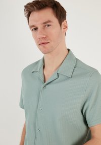 Lichtgroen shirt met korte mouwen, voorzien van een geribbelde textuur, een notch-kraag en drie knopen aan de voorkant. Casual pasvorm en lichtgewicht stof.