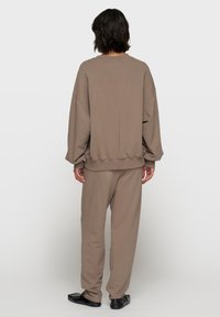Brązowy, oversize'owy sweter z prążkowanymi mankietami i dołem, w zestawie z dopasowanymi, luźnymi spodniami, obie części wykonane z miękkiego materiału. Założone płaskie buty.