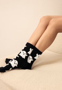 Zwarte sokken gemaakt van zacht materiaal met een patroon van witte spookvormen met zwarte gezichtsdetails. Enkelhoog, comfortabel ontwerp.