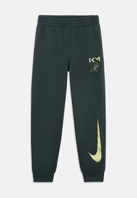 Nike trenirke v temno zeleni barvi, s elastičnim pasom, stranskimi žepi in Nike logo z valovitim vzorcem v rumeni barvi.