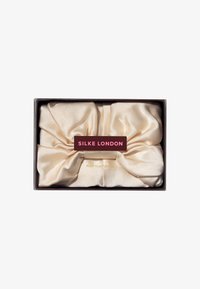 Ren silke turban i bløt beige, med en glatt tekstur og rund sløyfedesign. Pakket i en rektangulær boks merket "SILKE LONDON."