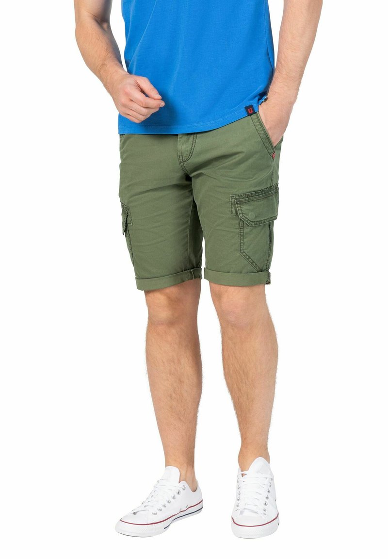 Grüne Cargo-Shorts mit umgeschlagenen Säumen, zwei seitlichen Taschen und einer Gesäßtasche, aus leichtem Stoff. Kombiniert mit weißen Turnschuhen.