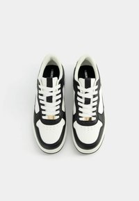 Black and white sneakers with leather upper, flat white laces, gold accent on the tongue, perforated toe, and cushioned sole.