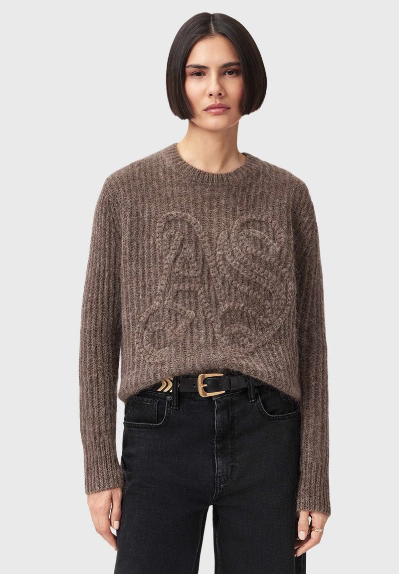Brun strikket sweater med ribbet tekstur og store præget bogstaver på fronten. Kombineret med sorte jeans og et sort bælte.