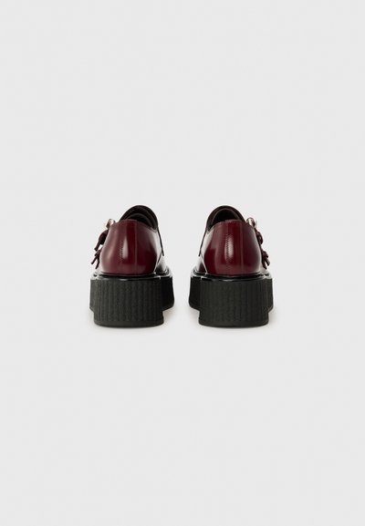 Scarpe in pelle bordeaux con una robusta suola nera a piattaforma. Presentano una finitura liscia e un dettaglio a fiocco sul retro. Design a punta arrotondata.