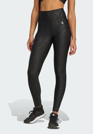 Leggings neri con un motivo a zebra testurizzato e tonale. Presentano un alto busto e dettagli di cucitura. Abbinati a scarpe da atletica nere.