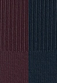 Une vue en gros plan d'un tissu texturé, divisé verticalement en bleu foncé à droite et en bordeaux à gauche, mettant en valeur de fins motifs côtelés.