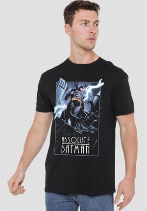Man wearing black t-shirt with a graphic of Batman standing on a rooftop with lightning in the background and text "Absolute Batman."