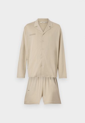 Light beige pajama set composed of a button-up long-sleeve shirt with a chest print and matching shorts, featuring an elastic waistband.